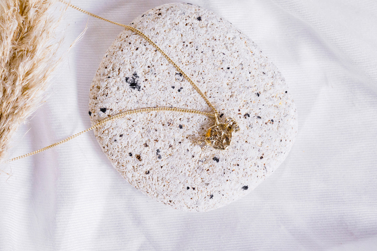 round solid yellow gold pendant with three white sapphire accents on a gold chain styled on a white background, rock and pompass grass