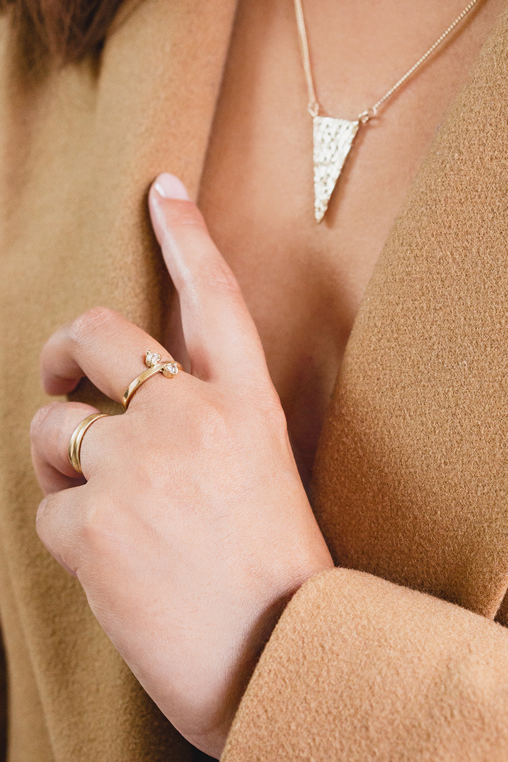 14 karat yellow gold ring with two white lab sapphires modeled by a hand resting on camel jacket lapel