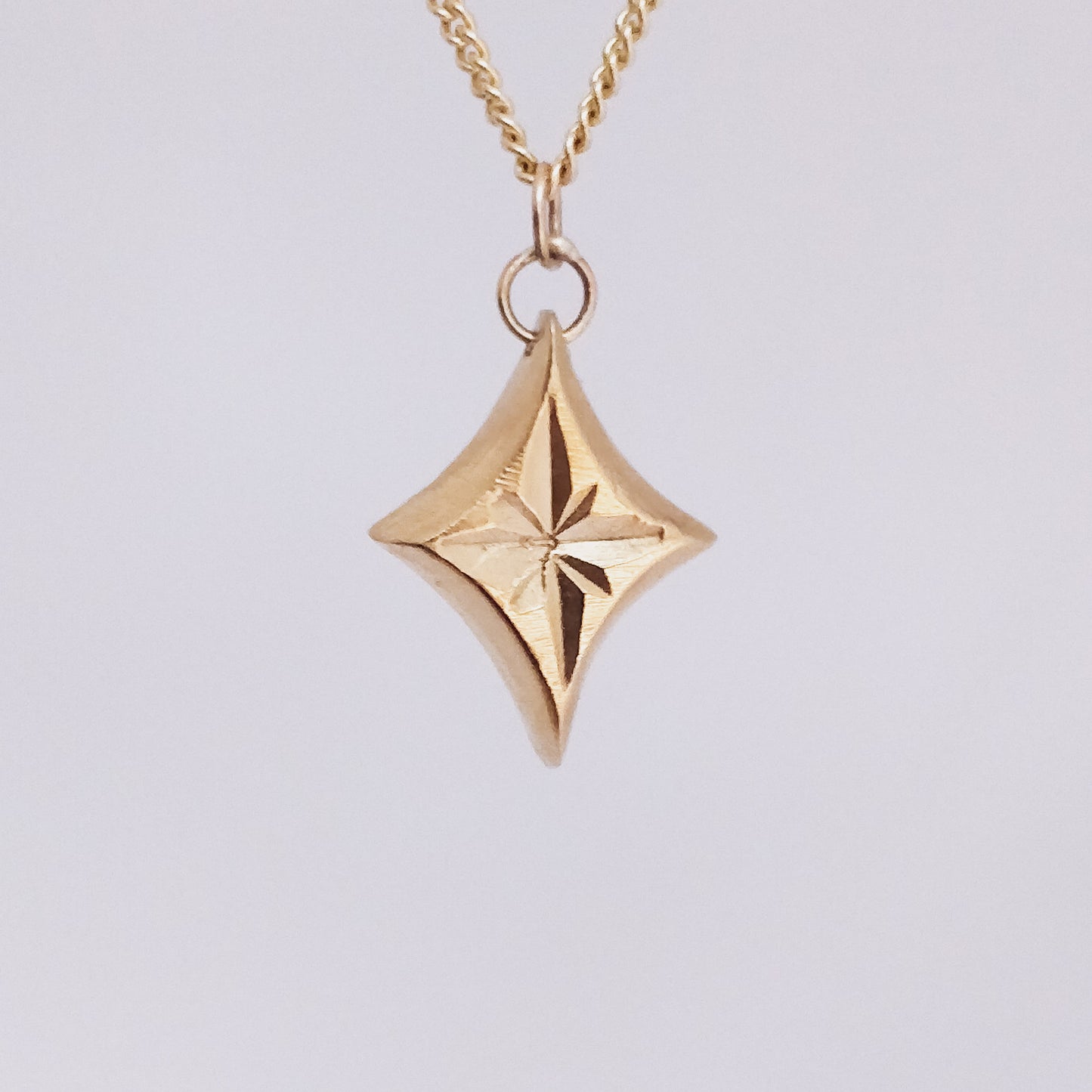 closeup of star engraved yellow gold pendant necklace on a white background