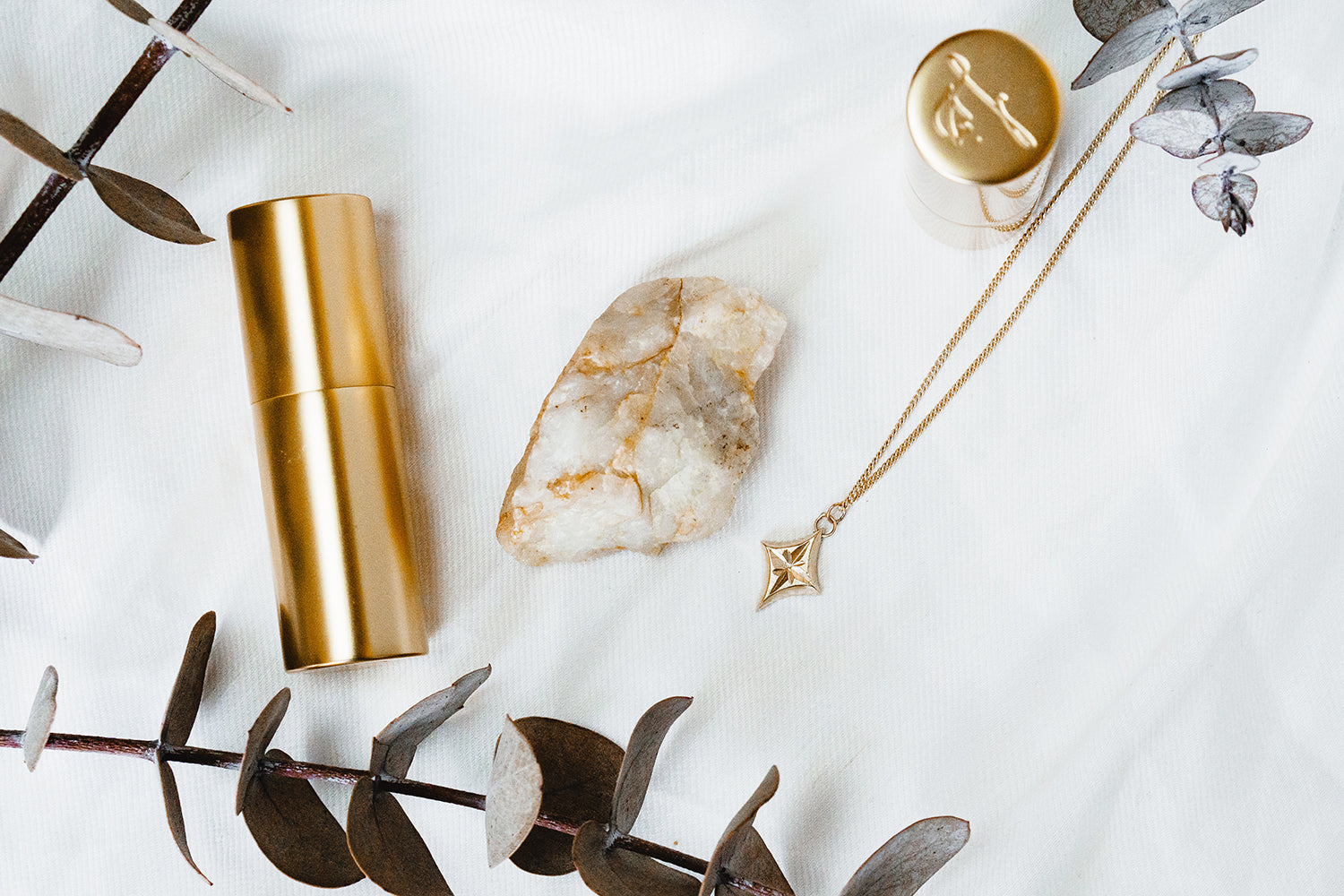 star engraved yellow gold pendant necklace styled in flatlay with lipstick bullets crystal rock and eucalyptus leaves