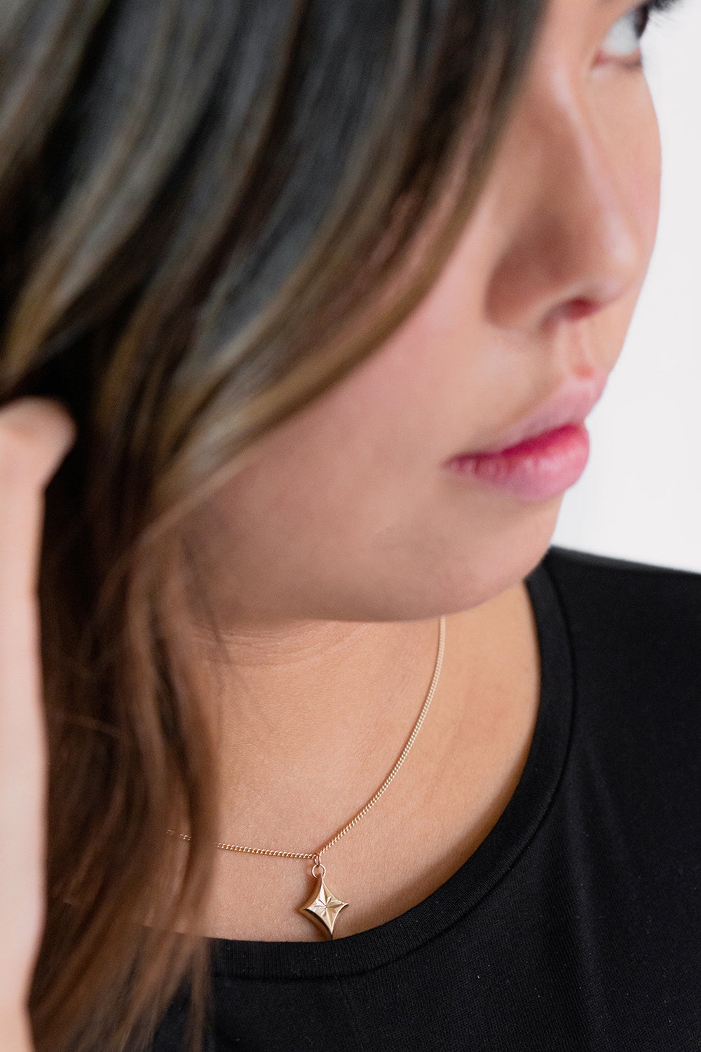 star engraved yellow gold pendant necklace worn alone on model with black top