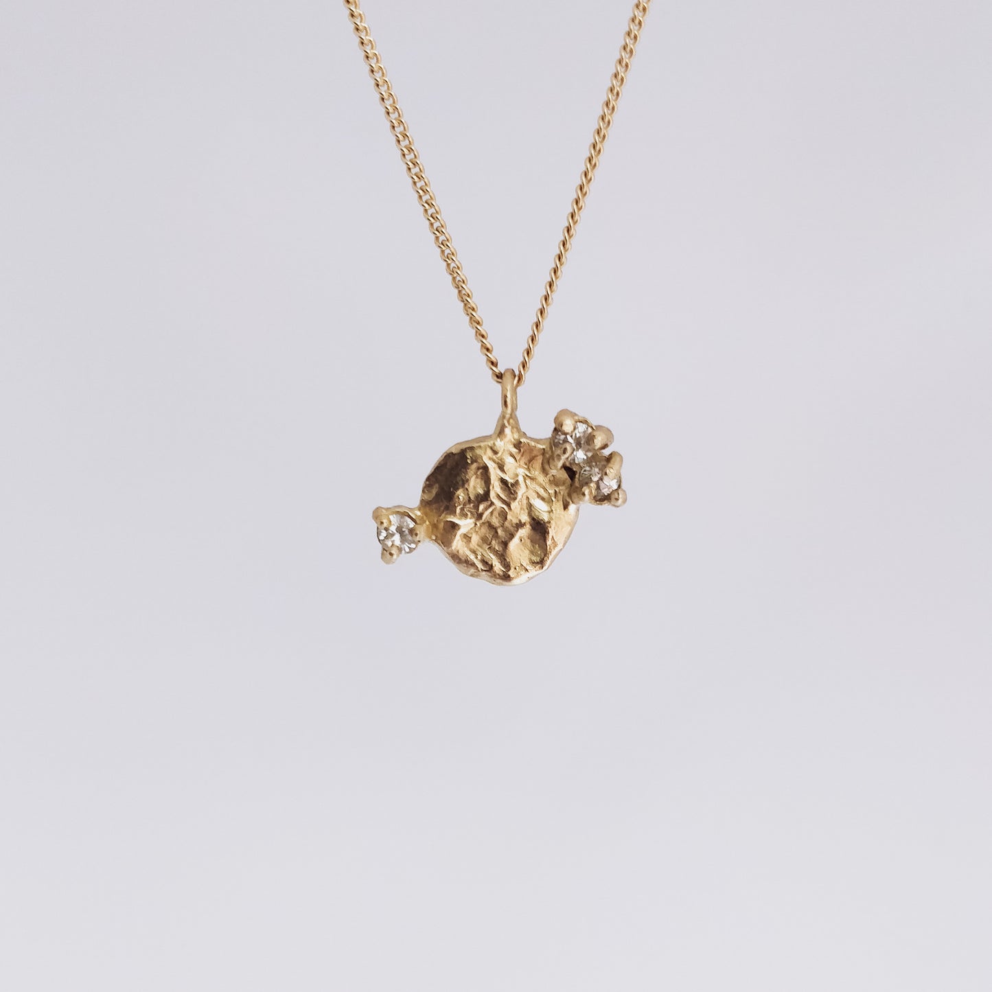 textured round yellow gold pendant with three white sapphires on a gold chain on white background