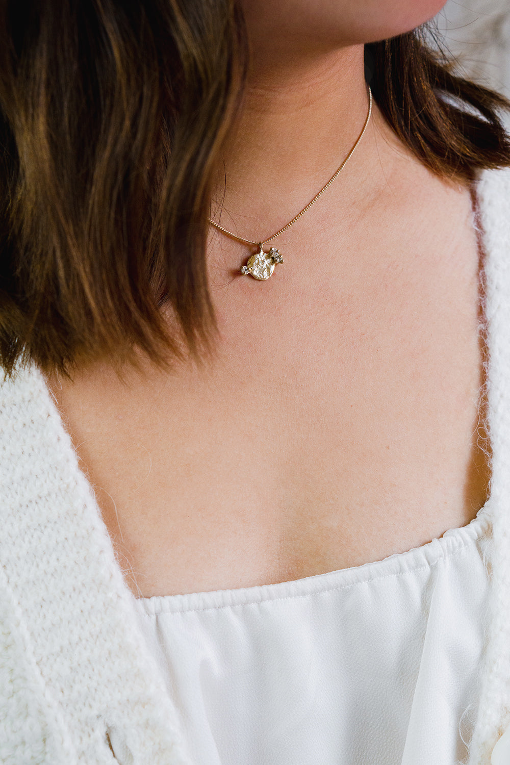 textured round yellow gold pendant with three white sapphires on gold chain styled on model wearing white cardigan and white top